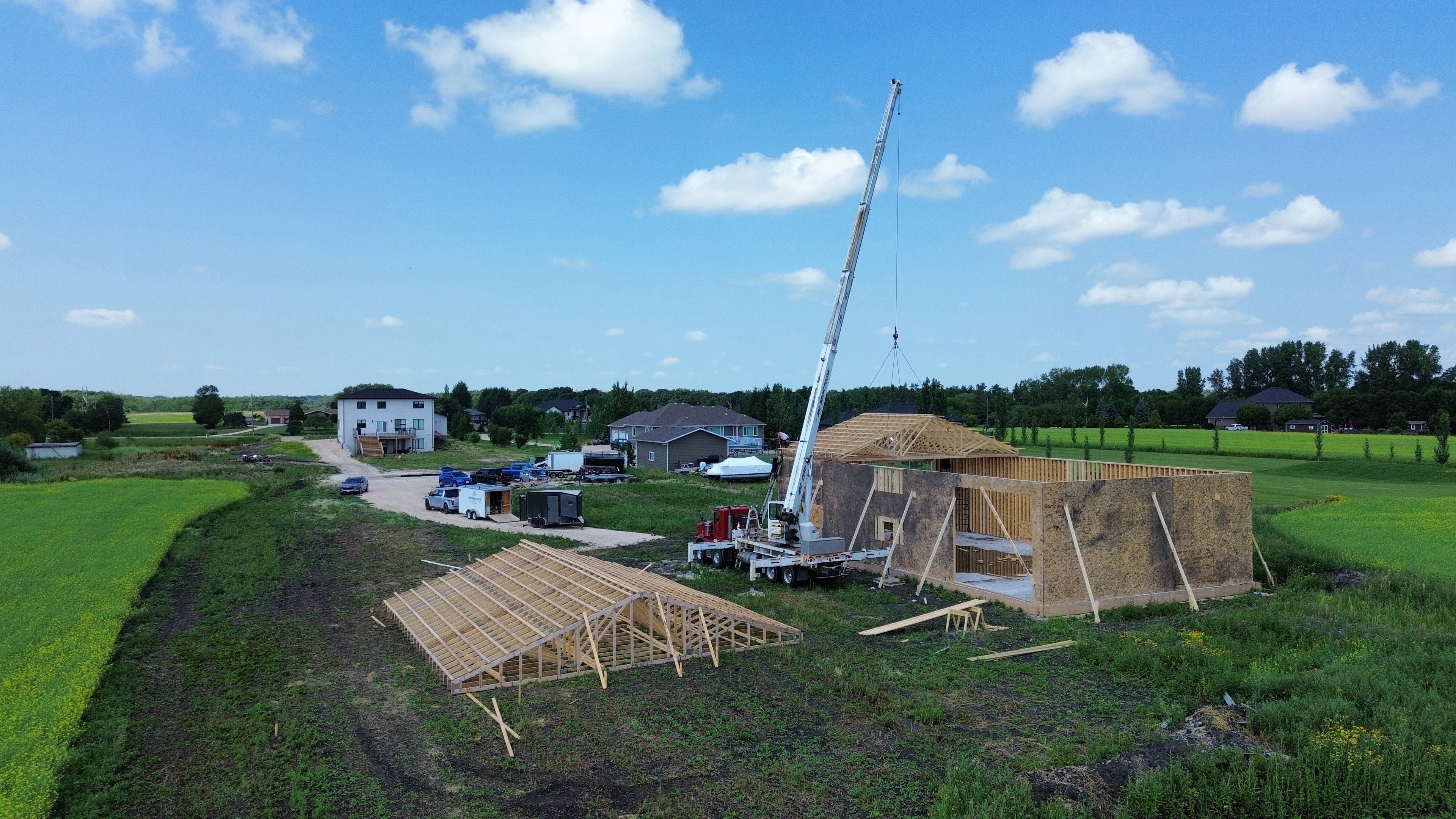 Rural shop build — aerial view, trusses laid out, crane on site